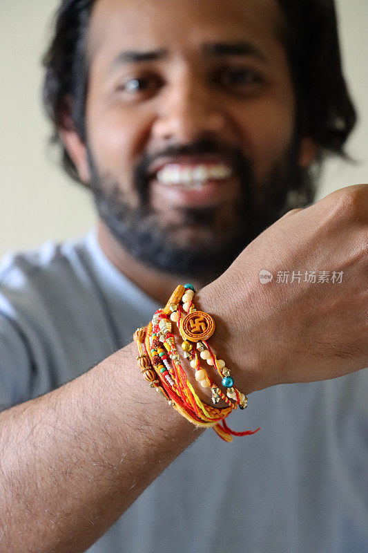 Raksha Bandhan印度教的兄弟情谊和爱的节日，一个印度人微笑着看着相机手腕上的rakhi串手镯的图像，重点放在前景